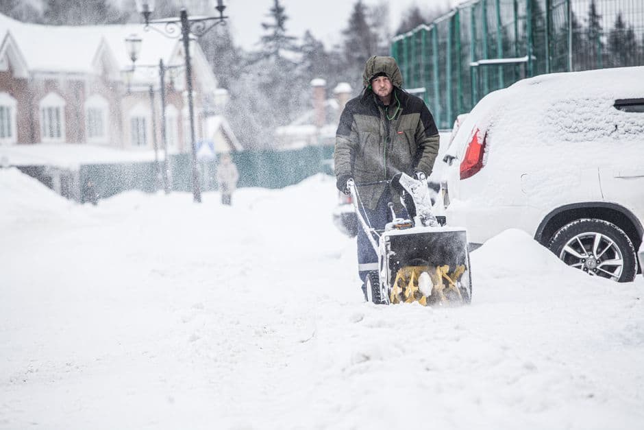 A man using a snow blower to clear snow from a snowy street in winter