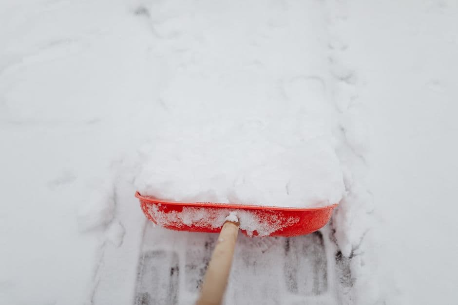 Close-up of a red shovel clearing snow from a driveway in winter