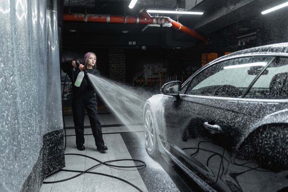 A person using a pressure washer to clean a car in a garage setting