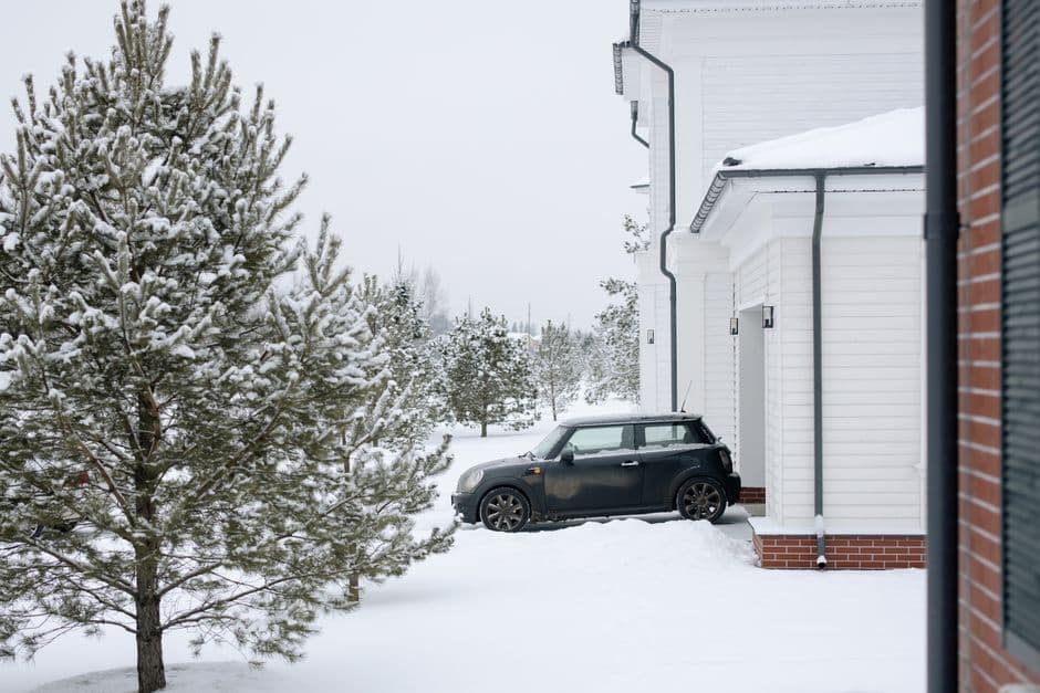 A car parked in a snowy driveway beside a white house during winter